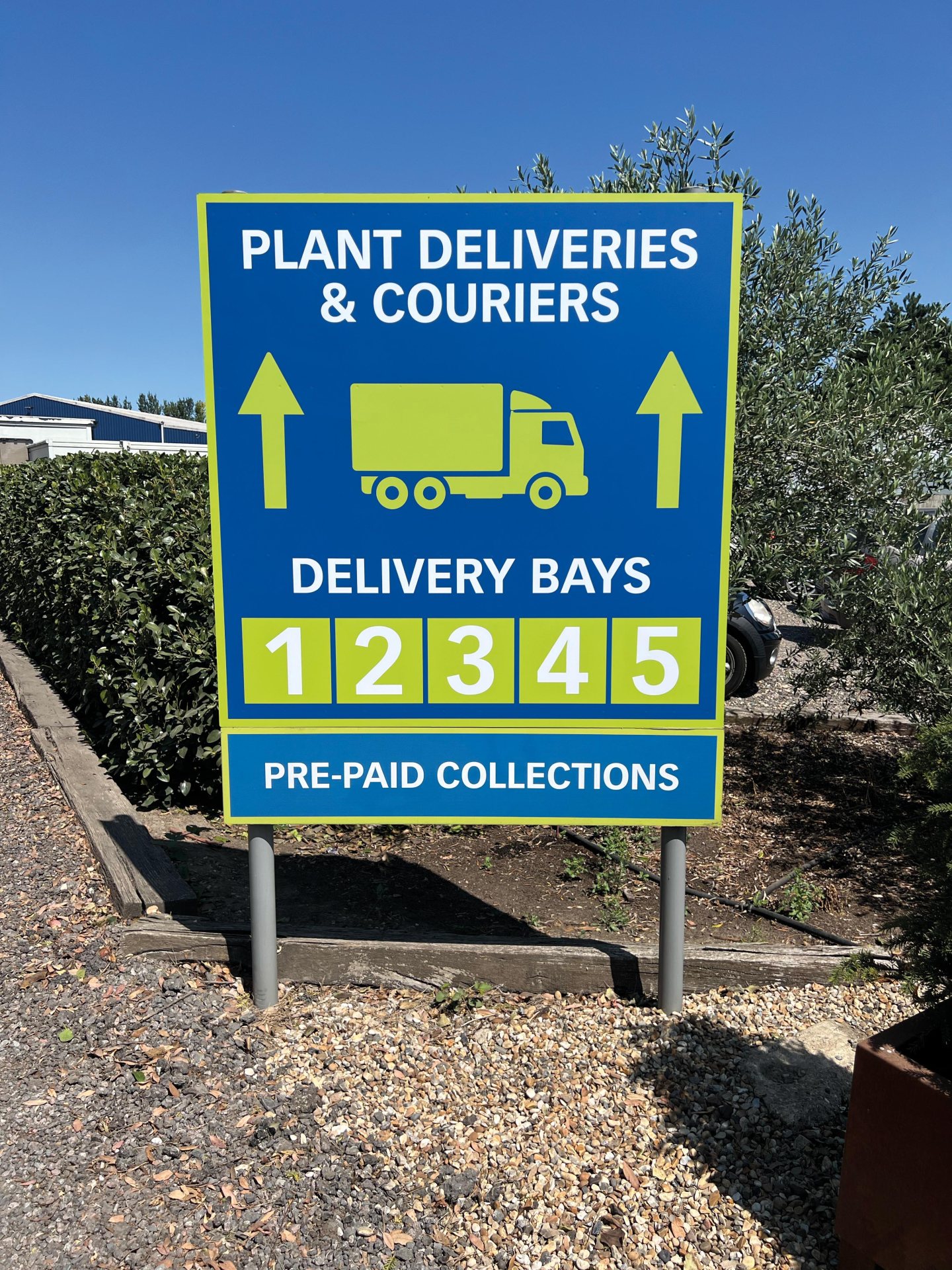 Blue and lime green post-mounted directional sign for plant deliveries, couriers and pre-paid collections, showing delivery bay numbers and arrows.