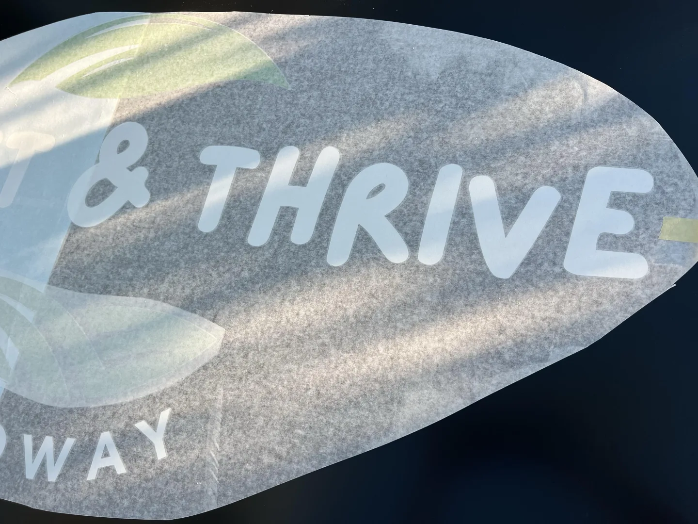 White matt vinyl lettering and green leaf graphics for Thrift & Thrive Medway being applied to a black ACM shopfront sign beneath translucent application tape.