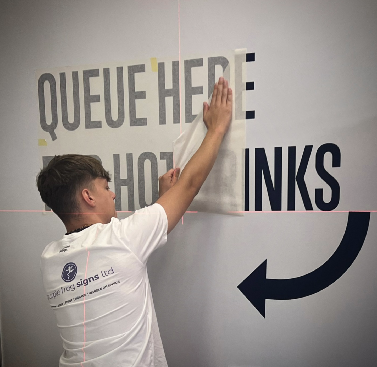 Purple Frog Signs installer applying directional vinyl wall graphics inside a global corporate building.